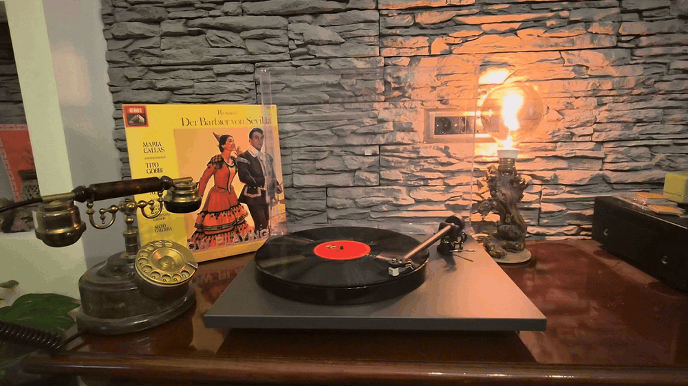 Gramofon sa pločom koja se okreće, pored starinskog telefona i lampe uz kameni zid