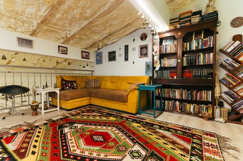 Prostrana soba sa žutom sofom, velikom bibliotekom i šarenim ćilimom